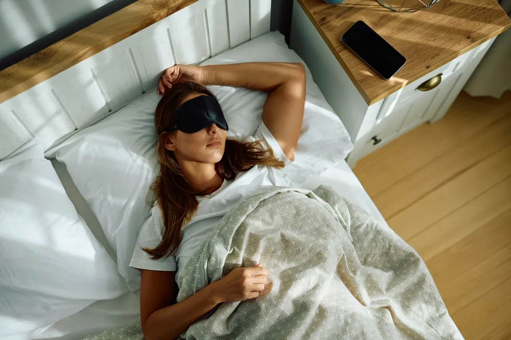 Ilustračná fotografia ženy odpočívajúcej v posteli s maskou na oči.